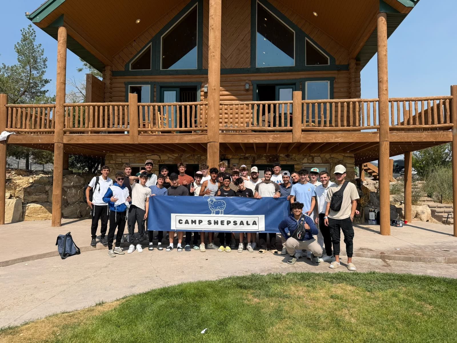 Camp Shepsala group holding its banner in front of a log lodge