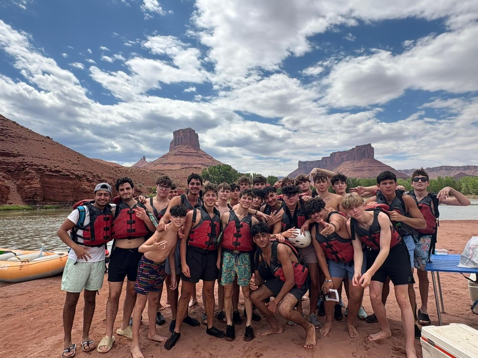 Camp Shepsala group wearing river safety gear beside red canyon cliffs
